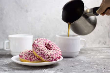 two donuts on a plate and womans hand pours coffee from cezveの写真素材