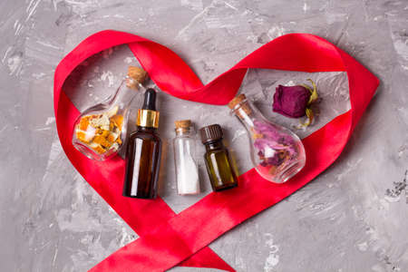 Spa concept of love for your body: heart shaped red satin ribbon aroma oils bottles,sea solt, dry rose petals and orange peel for scrubの写真素材