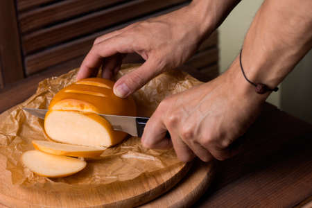 close up of men's hands  with a knife cut smoked homemade cheeseの写真素材