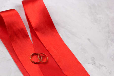 two golden rings and red satin ribbon wedding decor or wedding invitation background conceptの写真素材