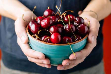 close up man hands with cherries in ceramic bowl