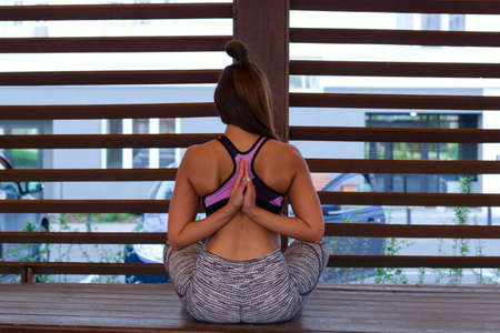 rear view of girl in the Lotus position hands in a Namaste sign behind the back