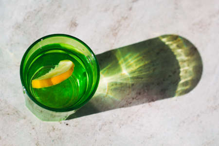 top view bright glass with drink and lemon slice, beautiful shadow on a stone marble table  ,detox, creativity,fashion conceptの写真素材