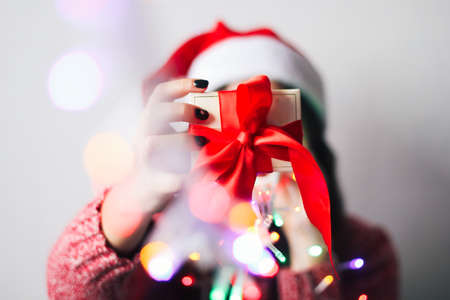 beautiful young woman with shining garland lights  and gift box with red satin ribbon