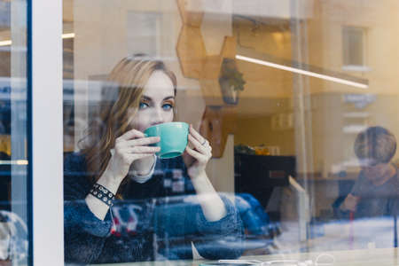 beautiful smiling young woman in gray sweater using mobile phone with earphones in cafe