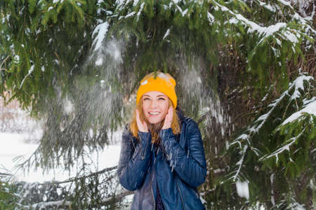 cute happy woman in yellow hat under snow fall in winter forestの写真素材