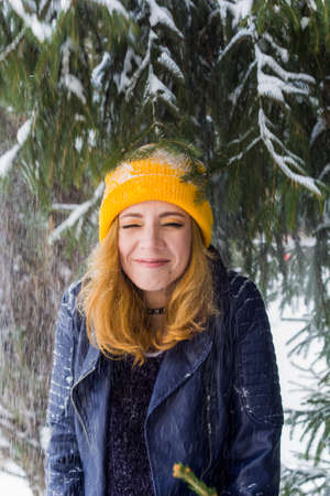 cute happy woman in yellow hat under snow fall in winter forestの写真素材
