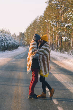 cute couple of handsome young man and beautiful young woman under woolen plaid in winter forestの写真素材