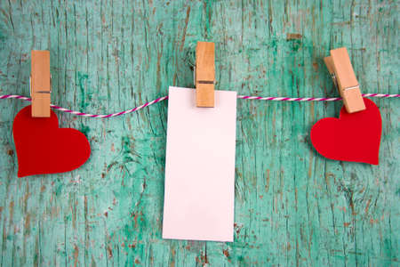 white  blank label with place for text and paper red hearts hung on clothespins on a rope on a mint green wall backgroundの写真素材