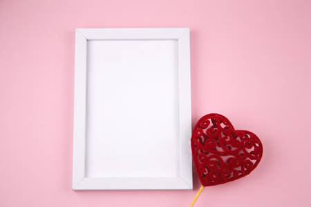 empty white wooden frame and red heart on a pastel pink background