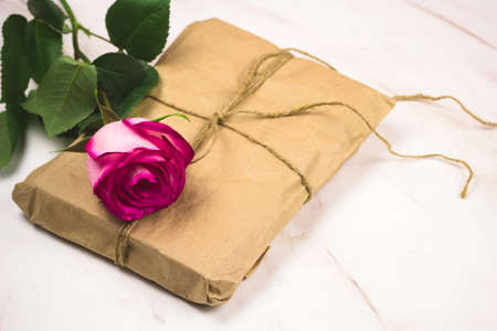 pink rose and present box wrapped  in vintage paper on a marble background