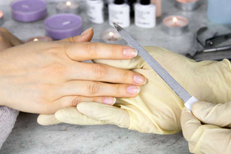 close up hands of manicurist in gloves with  nail file holding  hands of  client,  process of manicure and nail care in beauty salonの写真素材