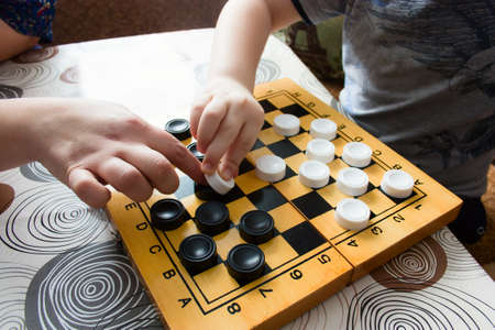 unrecognizable  woman and kid playing checkers at home,  closeup of a child's hand and mother's hand  moves figuresの写真素材