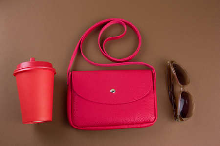 top view female bag, sun glasses and take away drink cup on brown background