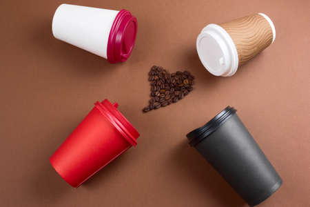 top view heart of coffee beans and various coffee drinks in paper disposable cups flat lay brown background, mock up blank paper cupsの写真素材