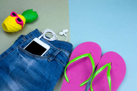 top view flat lay cute pineapple in sunglasses, blue denim jeans , smartphone and pink flip flops on a green and blue background, summer clothing set women's fashionの写真素材