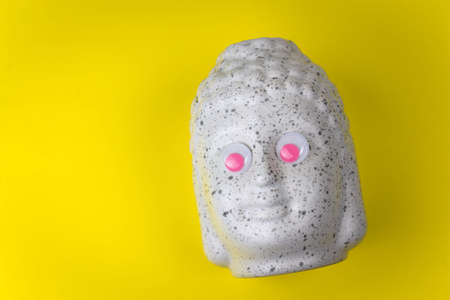 Buddha ceramic head with pink googly eyes on a yellow background