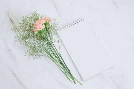 top view blank white notebook and boquet of carnation and gypsophila flowers on a marble backgroundの写真素材