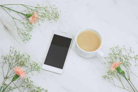 top view smartphone  and cup of drink with floral frame on a marble table