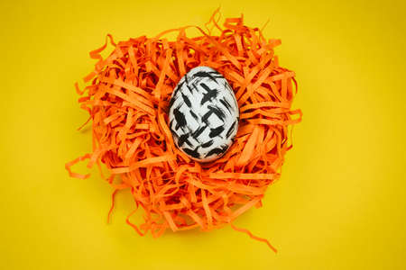 top view dyed black and white easter egg with geometric patetrn in decorative nest  on a yellow backgroundの写真素材