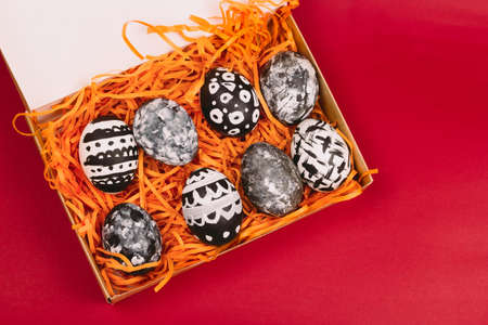 top view collection of dyed black and white easter eggs in box on a red background
