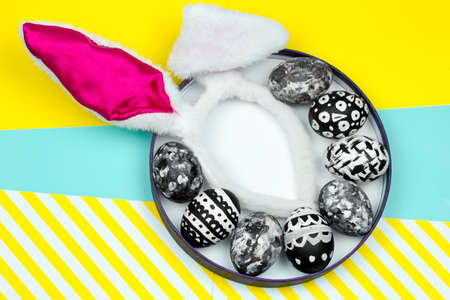 top view dyed eggs in a plate with bunny ears on a vibrant yellow and blue backgroundの写真素材
