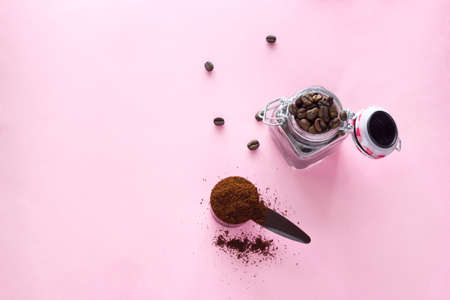 top view  spoon of ground coffee beans and jar with  coffee beans  on a pink backgroundの写真素材