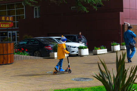 SOCHI,RUSSIA,  18 APRIL 2019 - boy in a bright yellow jacket riding a scooter in the park