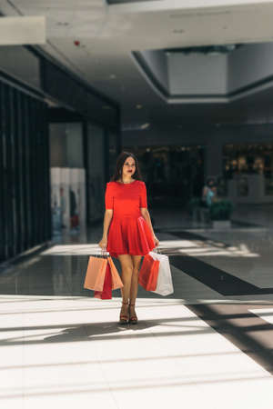 young beautiful woman in red dress with shopping bags walking around the mallの写真素材