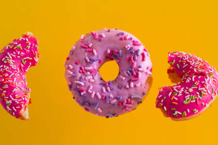 bright pink sweet donuts with sprinkles on vibrant yellow backgroundの写真素材