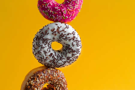 multicolored sweet donuts with sprinkles on vibrant yellow background copy space