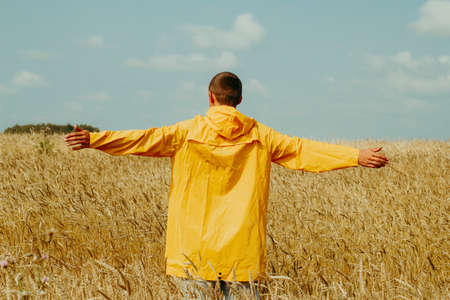 happy young man wearing yellow raincoat standing in a wheat field