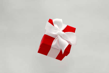 festive red gift box with white bow levitating isolated on a gray background