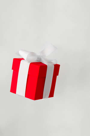 festive red gift box with white bow levitating isolated on a gray background