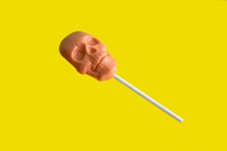 caramel on a stick in the shape of a skull on a yellow backgroundの写真素材