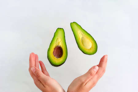 ripe fresh avocado slices fly into women's hands on white backgroundの写真素材