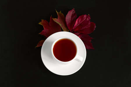 top view fall wallpaper with cup hot drink in a white cup and bouquet of autumn red leaves on a black table backgroundの写真素材