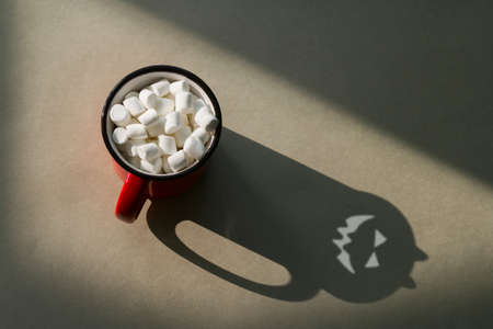 top view a mug of marshmallows and a frightening shadow with horns and a sinister faceの写真素材