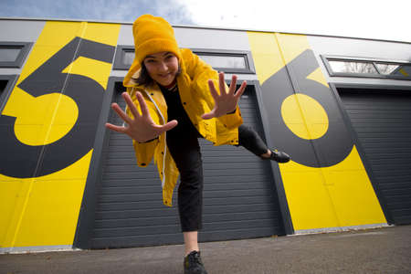 happy young caucasian woman wearing a yellow hat and a yellow raincoat dancing on a city street watching at the camera , positive active lifestyle and street fashion conceptの写真素材