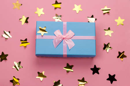 top view beautiful blue gift box with pink satin ribbon with bow on a pink background with golden stars sequinsの写真素材