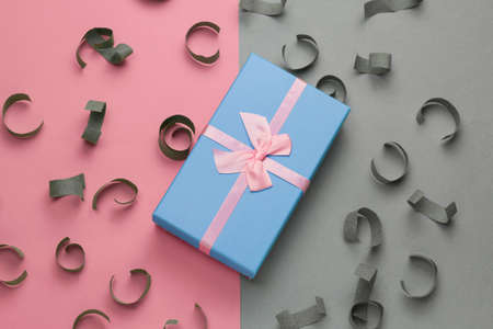 blue gift box with festive pink bow top view on a gray and pastel pink background with paper...