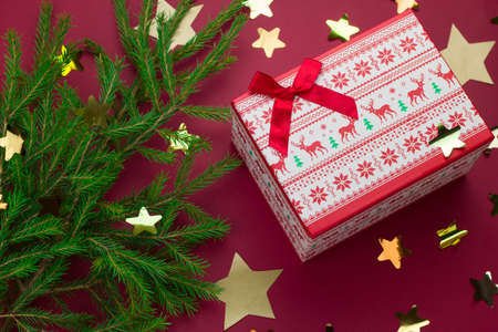 top view evergreen christmas tree branches, gift box and starry confetti on a red background