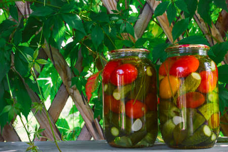 jars of pickled assorted tomatoes and cucumbers on the table in a wooden gazebo in the gardenの写真素材