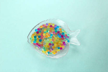 top view glass plate in the shape of a fish filled with colored balls of aqua grunt, ocean pollution microplastics conceptの写真素材