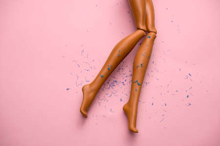 legs of a plastic doll with hair scattered on a soft pink backgroundの写真素材
