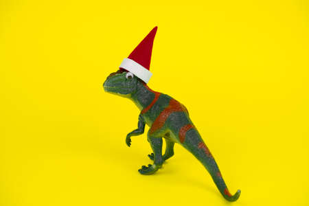 funny green dinosaur toy in little santa claus hat  on vibrant yellow backgroundの写真素材