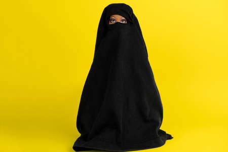 A doll in a black robe with a closed face on a yellow backgroundの写真素材