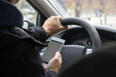 unrecognisable young male driver uses mobile phone while driving car