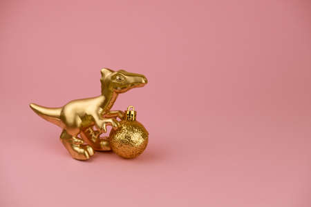 golden dinosaur toy with golden christmas ball on a pastel pink background, trendy modern christmas card with copy spaceの写真素材