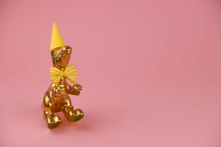 golden dinosaur in a perty hat and bowtie on a pink background with copy spaceの写真素材